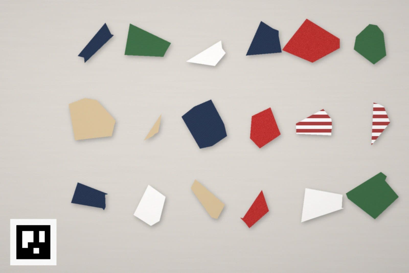 Eighteen fabric offcuts in navy, green, red, white, tan and striped fabric laid out on a grey table, with a square black-and-white ArUco marker in the corner.